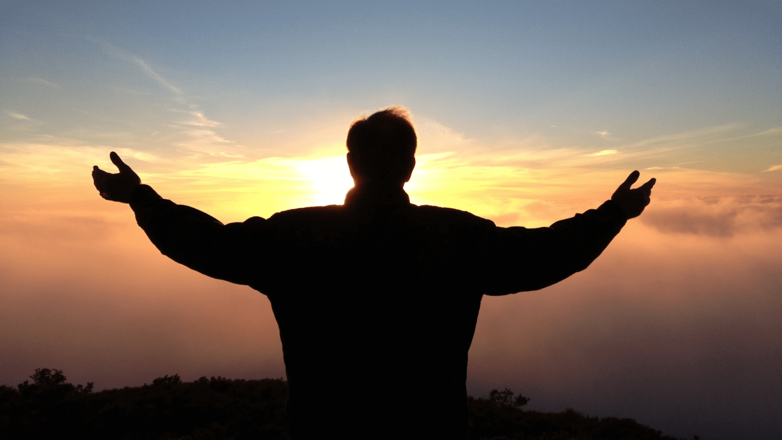 silhouette of a person with their arms out against a sunset background